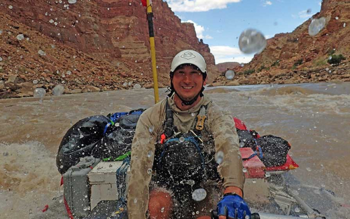 a person in a raft smiles as water splashes on an outward bound course